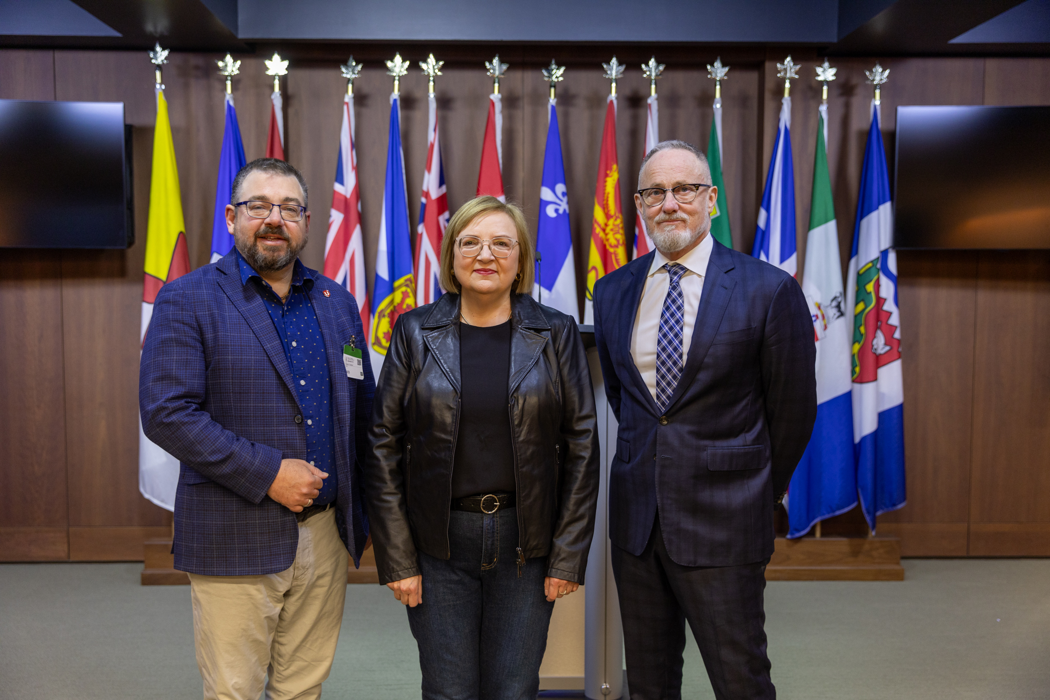 Three people standing in front of a row of provincial flags