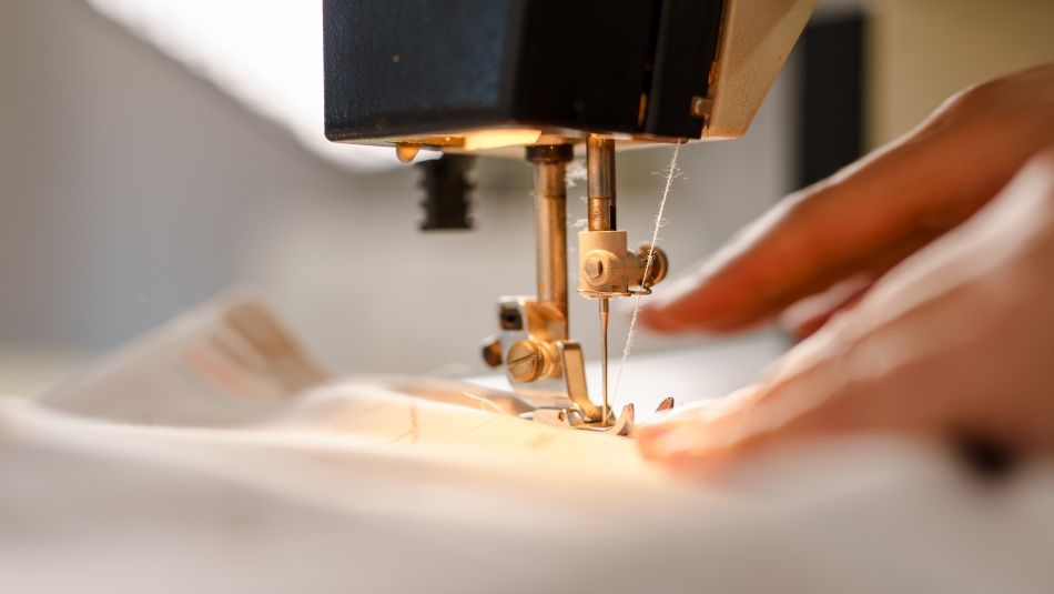 A garment worker's hands guiding fabric through a sewing machine 