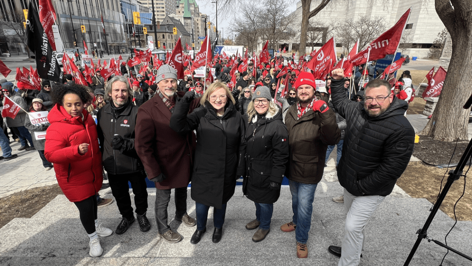 Unifor leadership stand in front with members with red flags in the background.