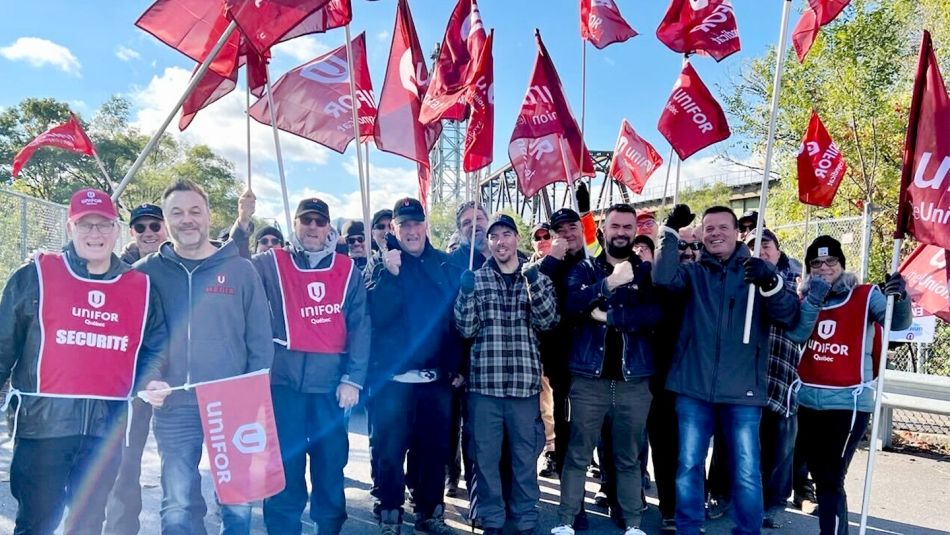 A group of Unifor members employed at the Saint Lawrence Seaway Management Corporation hold flags on a picket line.