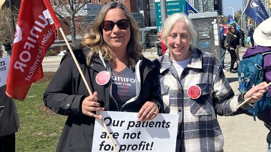 Two women at a rally at Grand River Hospital holding a place card and Unifor flag