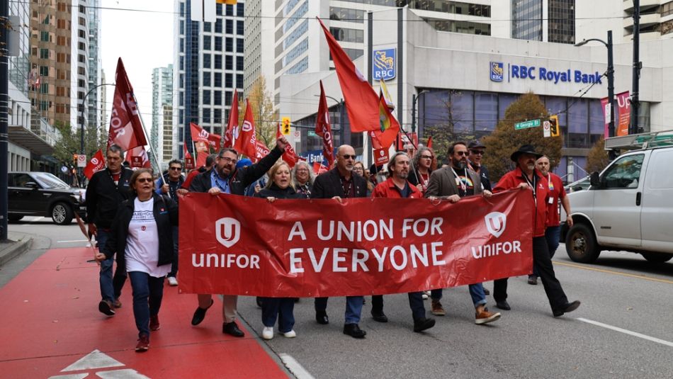 Des personnes défilent dans une rue de la ville avec des drapeaux et une banderole sur laquelle on peut lire Unifor : un syndicat pour tous.