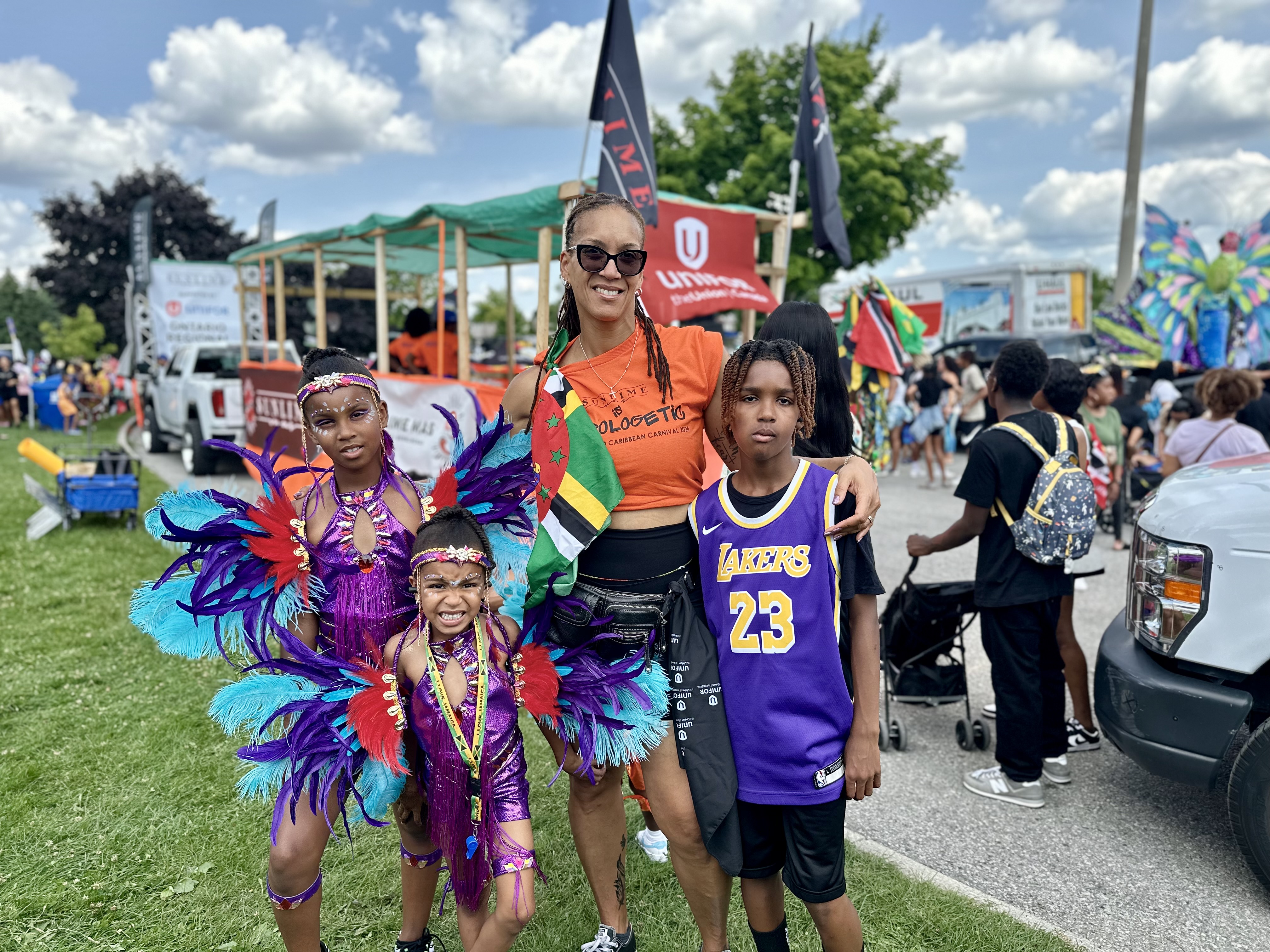 A woman with three kids, two in Caribbean costumes and one in a blue basketball jersey.