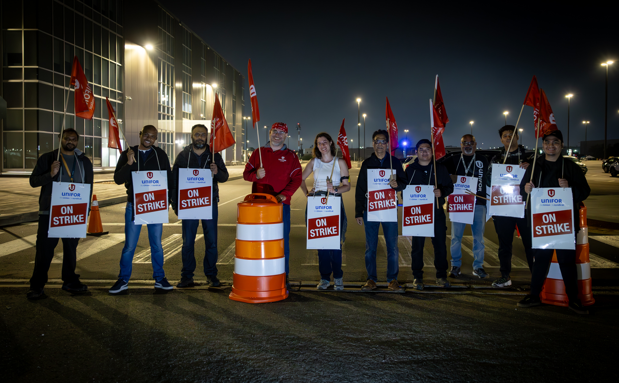 A group of Unifor members standing on the picket line wearing "on strike" signs and holding Unifor flags on the Bombardier picket lineholdin