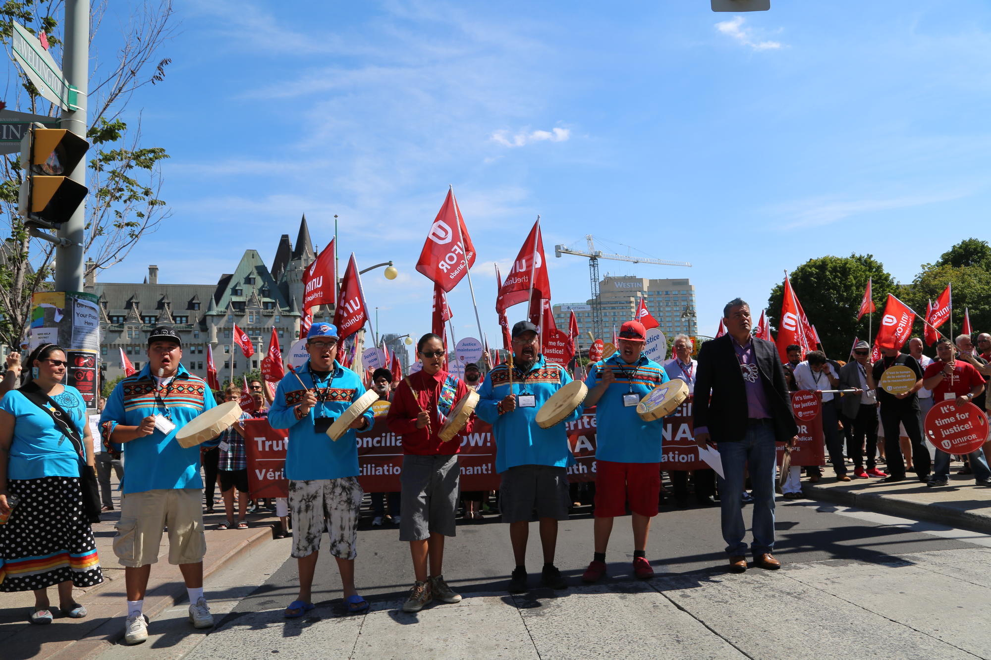 A row of indigenous drummers lead a group of Unifor activists at a rally.