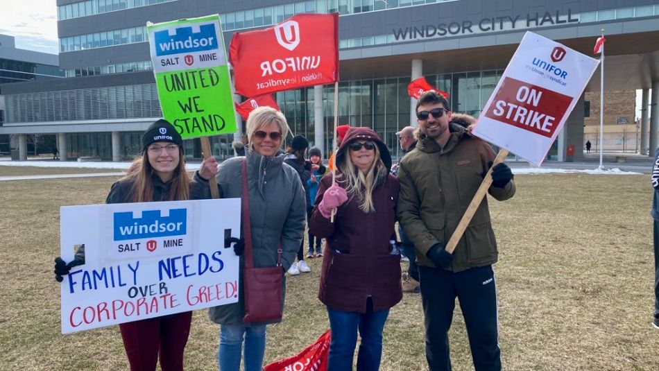 "Quatre personnes posant devant l'hôtel de ville de Windsor tenant des pancartes et des pancartes On Strike"