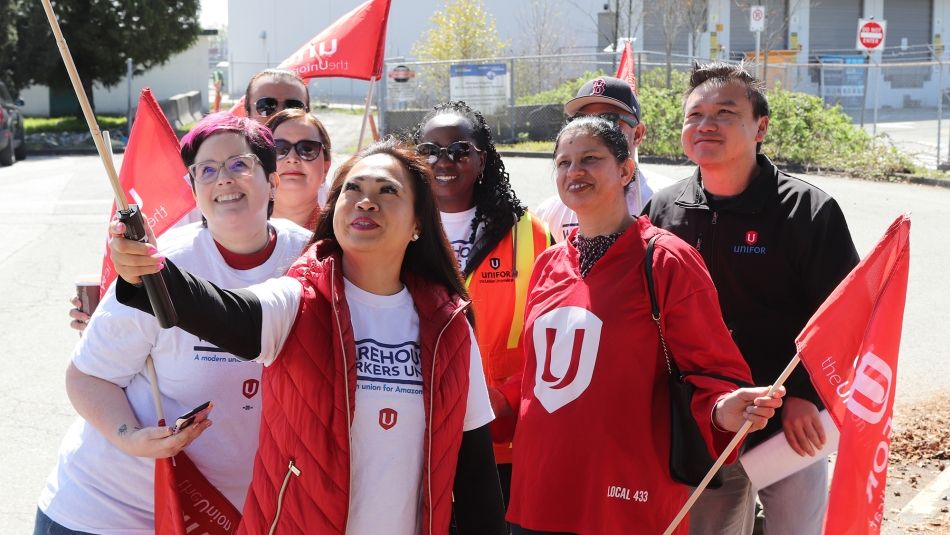 Un groupe de personnes prenant un selfie en portant l'équipement d'Unifor et en tenant des drapeaux d'Unifor. 