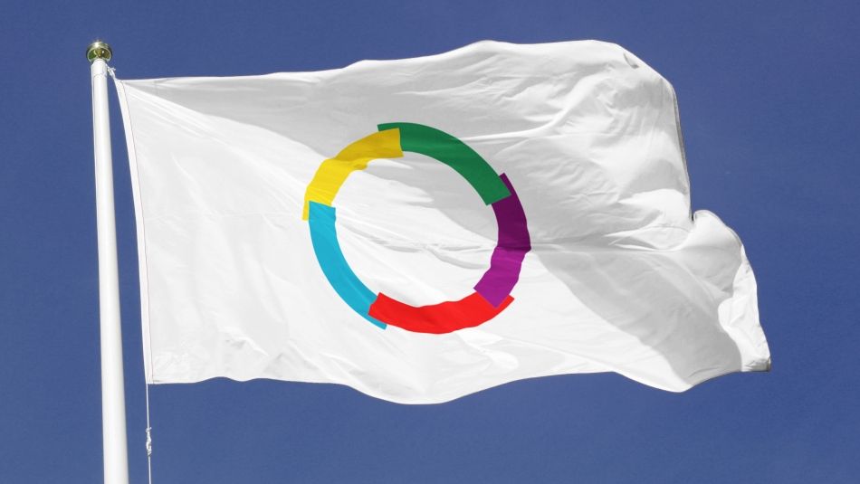 Flag of La Francophonie (multicoloured empty circle on a white background) waving against a deep blue sky.