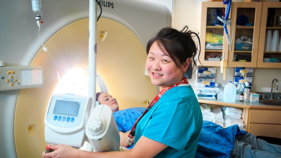 Une femme allongée sur un appareil de tomodensitométrie et une infirmière devant l'équipement médical. 