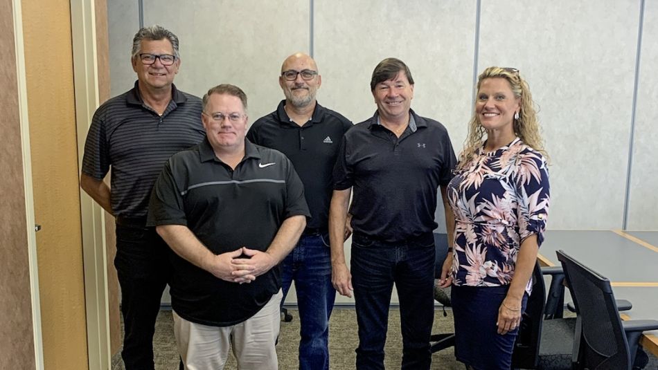 Five people in a meeting room standing and posing for a photo