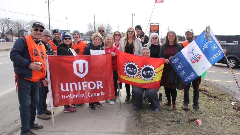 Unifor BC Leadership and members posing in front of a government sign on the picket line.
