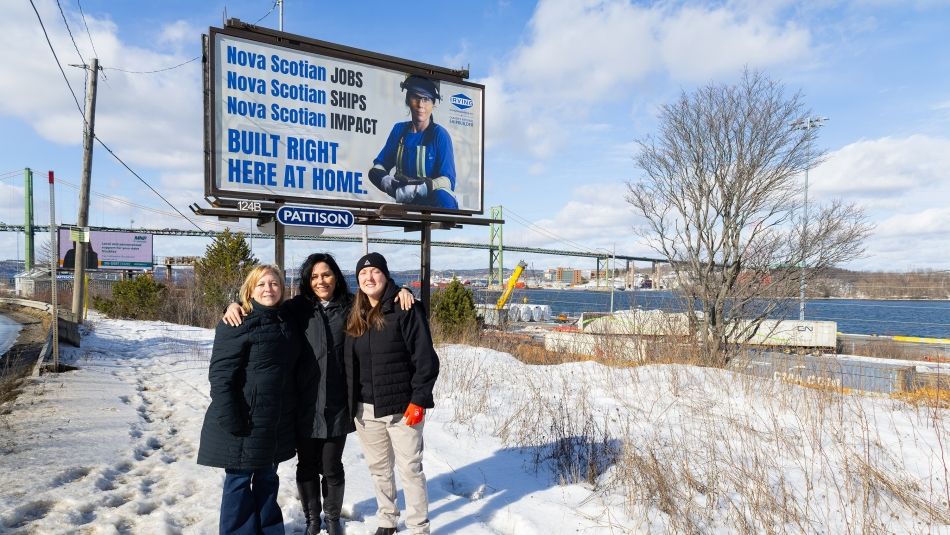Three women outside in the cold in front of a billboard