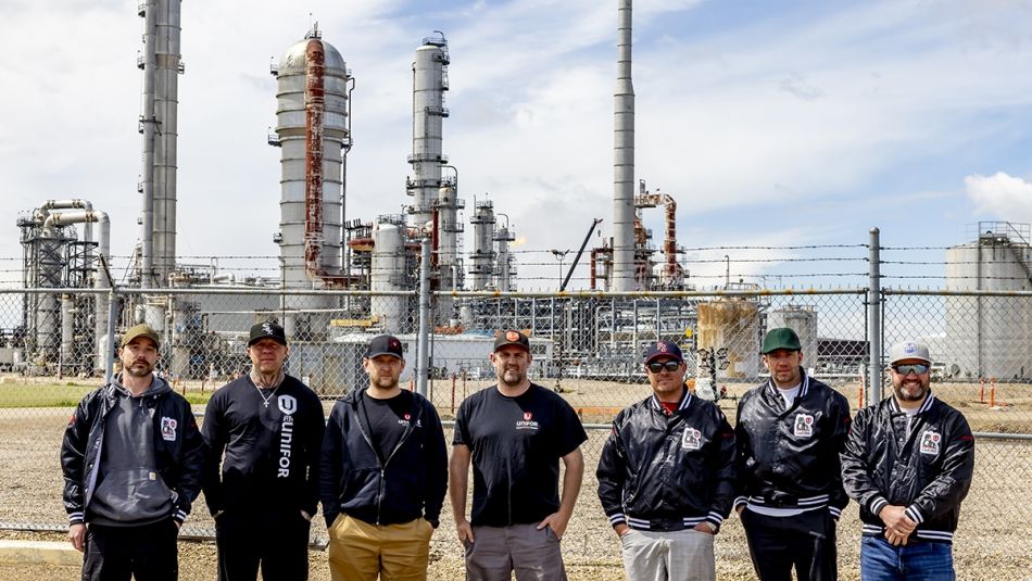 Seven people standing outside with a refinery behind them.