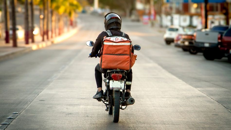 Rear view of a delivery driver on a motorcycle with an orange delivery crate.