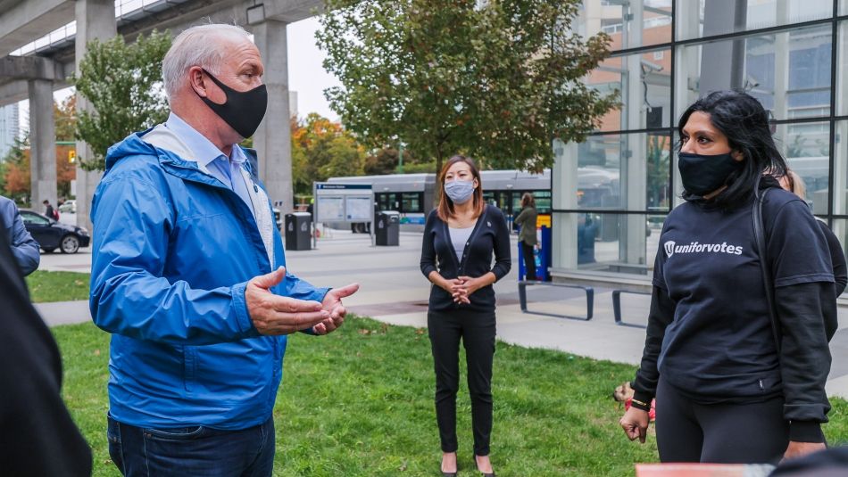 B.C. Premier John Horgan wearing a mask and speaking to a Unifor member outside of a Skytrain station in Vancouver