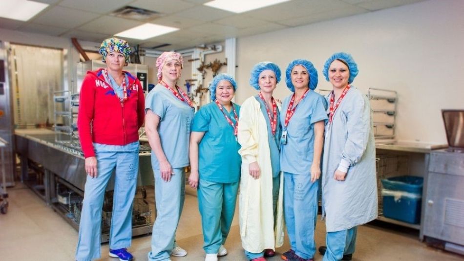Six nurses standing smiling wearing scrubs.