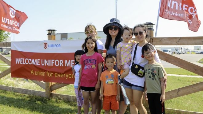 A family standing in front of a fence with a banner that reads: welcome Unifor members