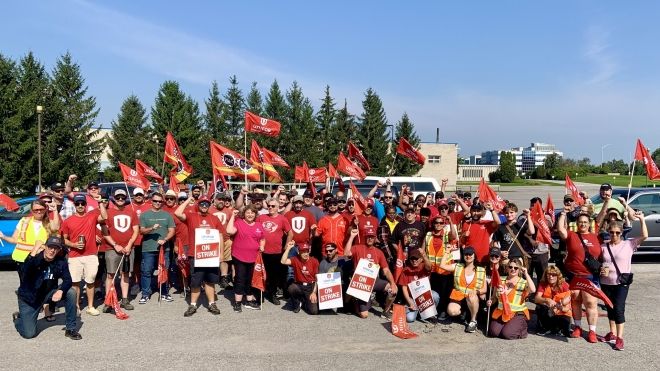 A large group of workers holding up placards and Unifor flags