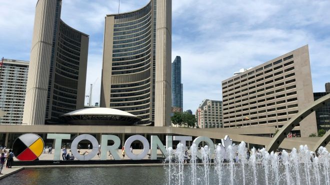 Wide view of two curved office towers and a dome that comprise Toronto City Hall with a fountain in the foreground