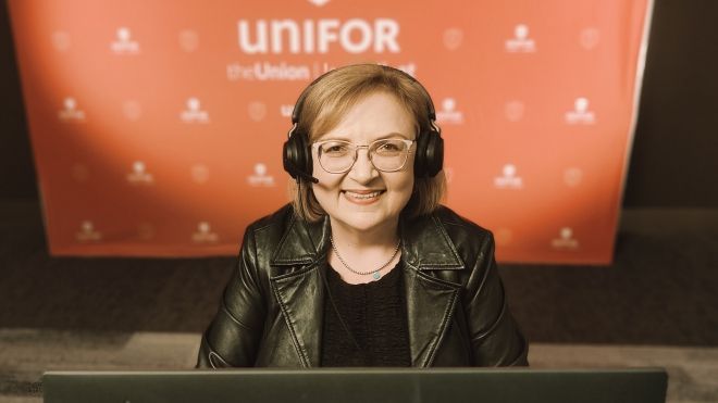 Women sits in front of a laptop and Unifor banner wearing headphones.
