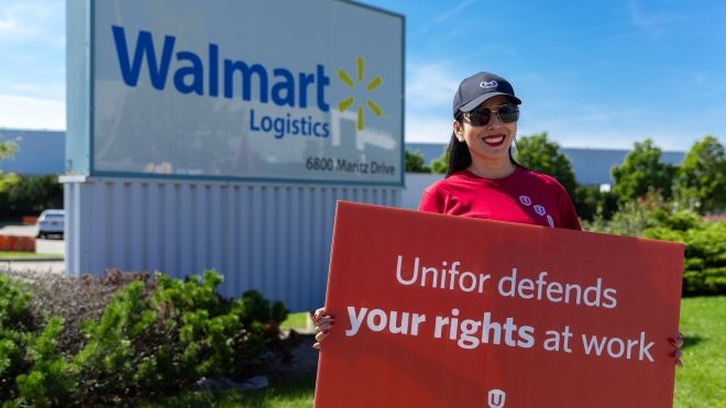 A woman standing outside a Walmart warehouse holding a sign that says Unifor defends your rights at work.