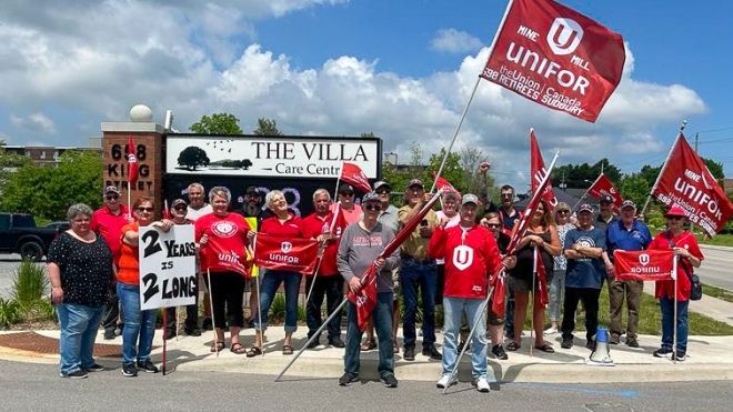 Unifor flags held by group of people in red unifor shirts next to the vila care centre 