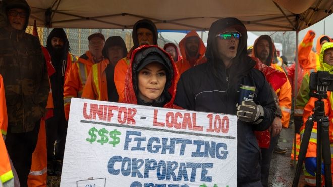 Un membre d'Unifor en grève tient une pancarte sur laquelle on peut lire "Les membres de la section 100 d'Unifor luttent contre la cupidité des entreprises" lors d'un rassemblement.