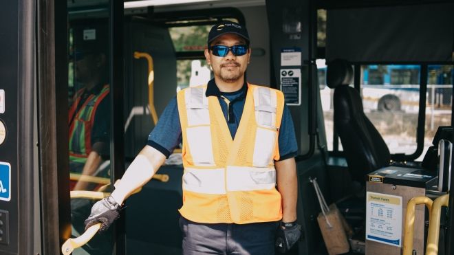 A man in a safety vest stands in the doorway of a transit bus