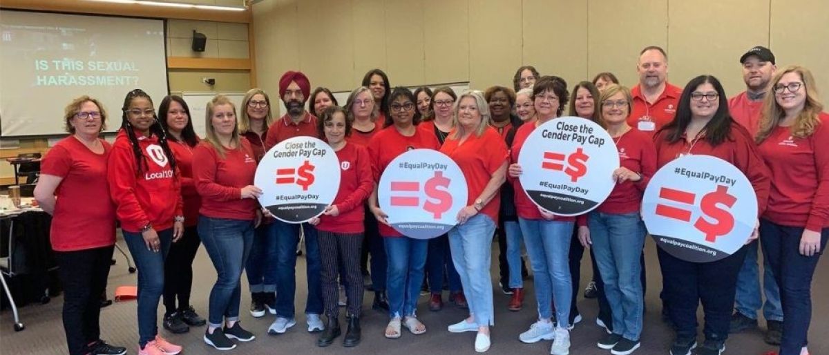 A group standing wearing red holding signs that read =$ 