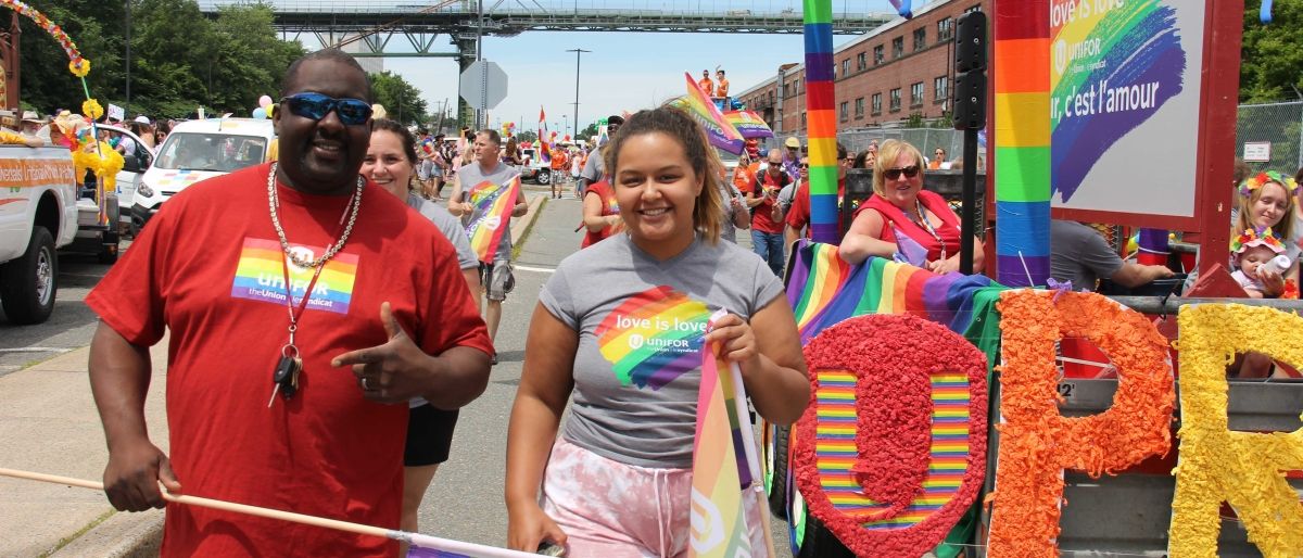 A black man and women march in the Halifax Pride parade in front of a colourful float